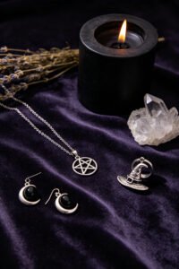 Witch jewelry collection with pentagram necklace, crescent moon earrings, black onyx ring and witch hat pendant on dark velvet